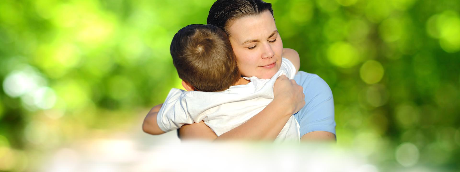 Woman hugging young son blurry green background