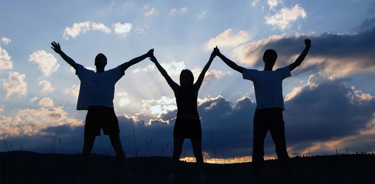 Three People Holding Hands In the Air Sunset