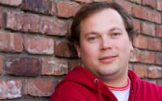 Middle aged man in red hoodie smiling brick wall