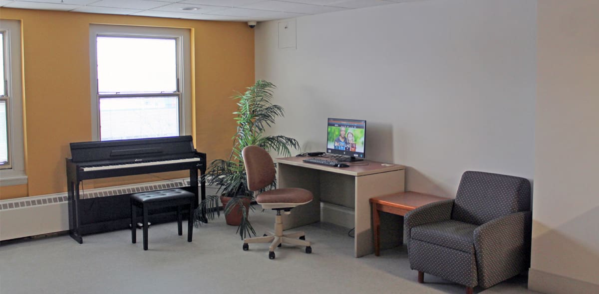 Room with yellow and white walls including chairs, computer desk and piano.