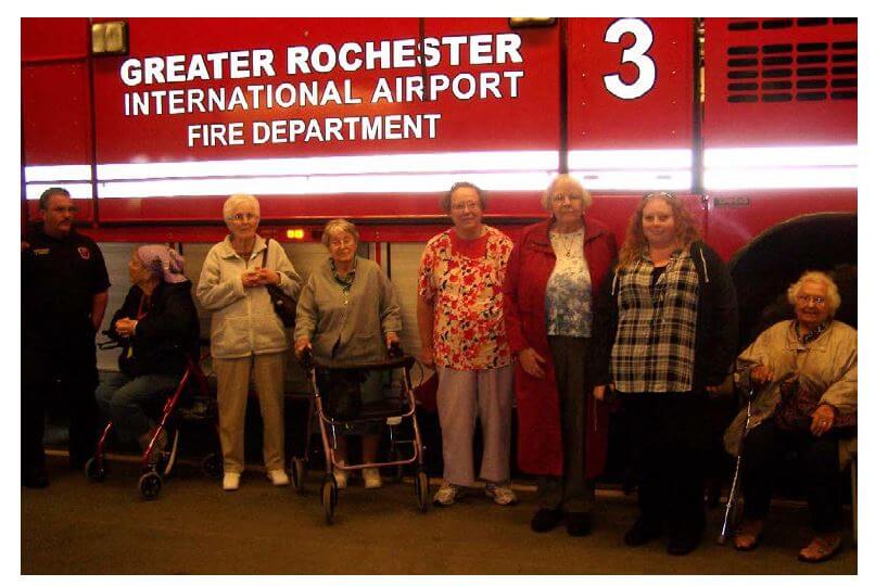 Woodcrest Commons residents Barb Frielinghaus, Joanne Hackett, Alma Coles, Kathy Hart, Anna Callon, Activities Director Lindsay Lown and resident Rosemarie Klos posing in front of a fire truck