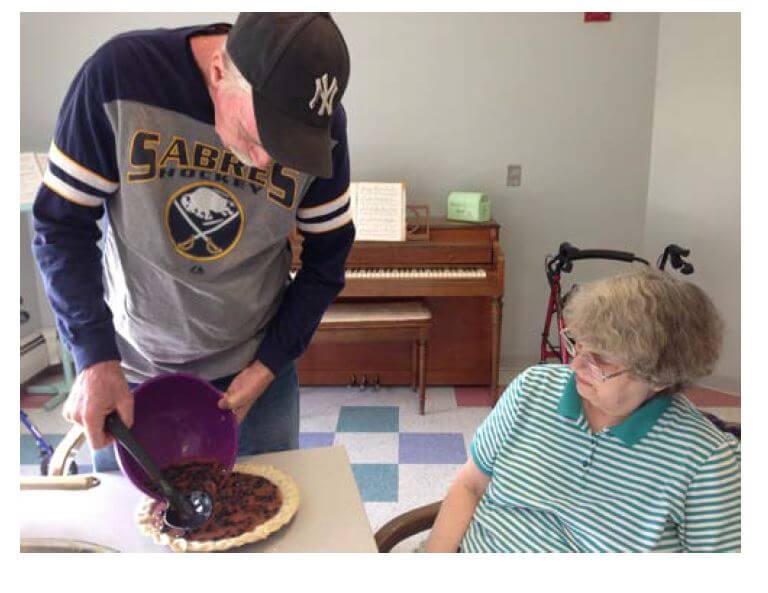 Woodcrest Commons resident Tom Armstrong pours the filling into a grape pie as Roseanne Bourne looks on