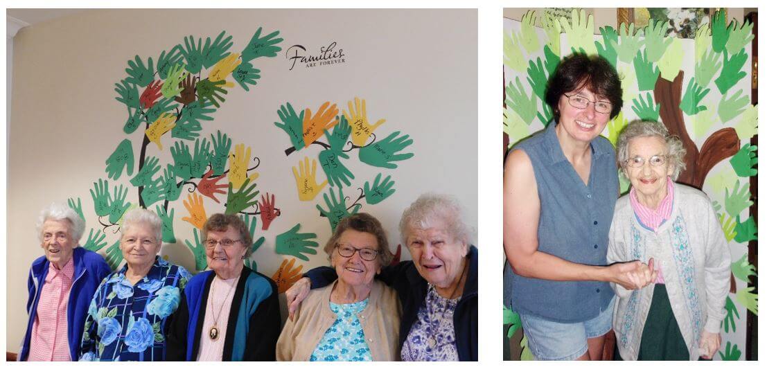 Residents and their family members posing in front of the trees made out of paper hands and thumb prints