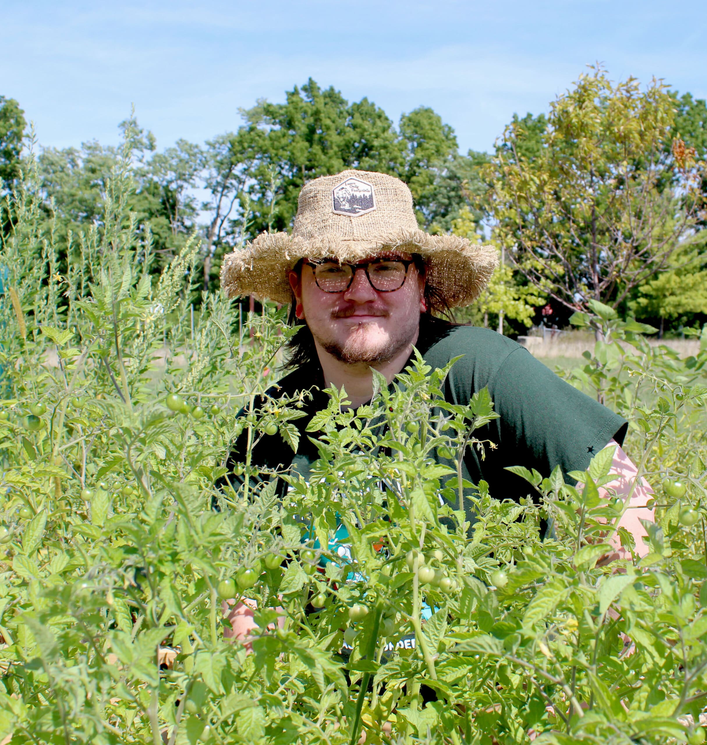 Garden in foreground; person wearing hat and glasses in background.
