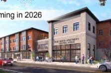 A modern three-story apartment building with a sign reading True North Apartments Central Avenue. People walk on the sidewalk, and cars are parked along the street. Text overlay says Coming in 2026. Trees with autumn leaves surround the scene.