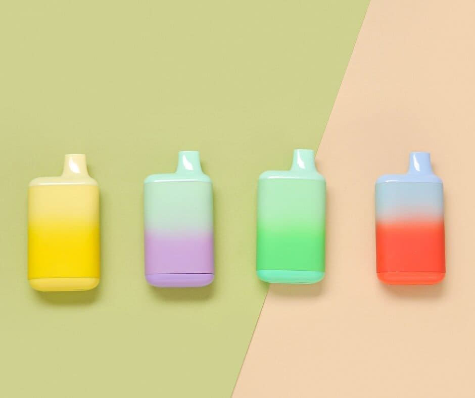 Four pastel-colored vape devices with gradient hues (yellow, purple, green, and red) are arranged side by side on a background split diagonally between light green and peach.